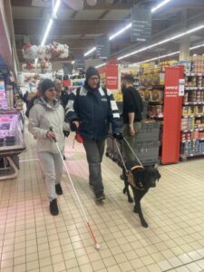 Tia guide en supermarché, deux personnes dont l'une avec une canne blanche
