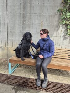 Trixie assise sur banc marron a cote de son maitre