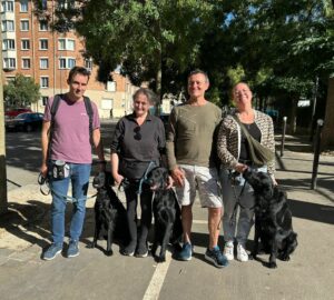 3 flatcoats noirs posent assis pres de leur FA et de l'éducateur Eric
