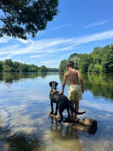 Aston est sur un rocher, de dos, sur un lac, à côté d'un enfant